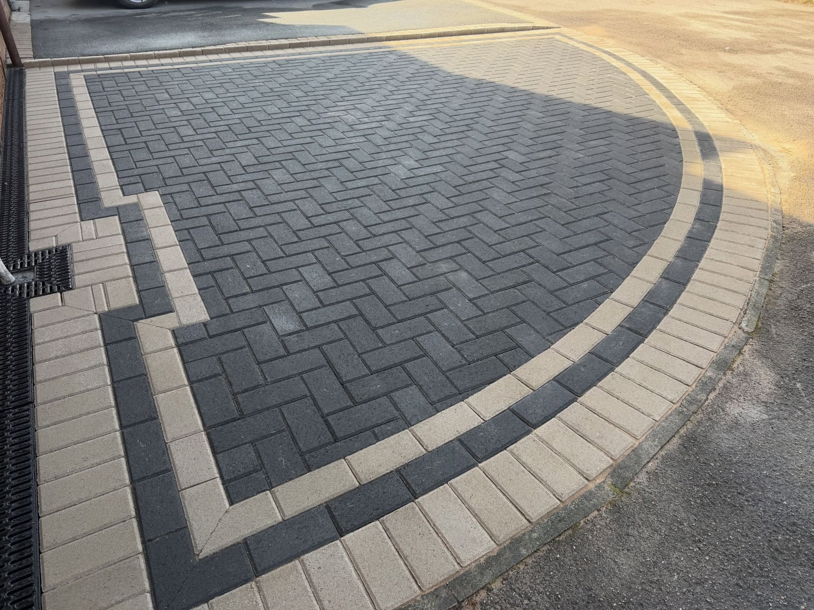 Sweeping buff and charcoal herringbone driveway border curves in Cheshire
