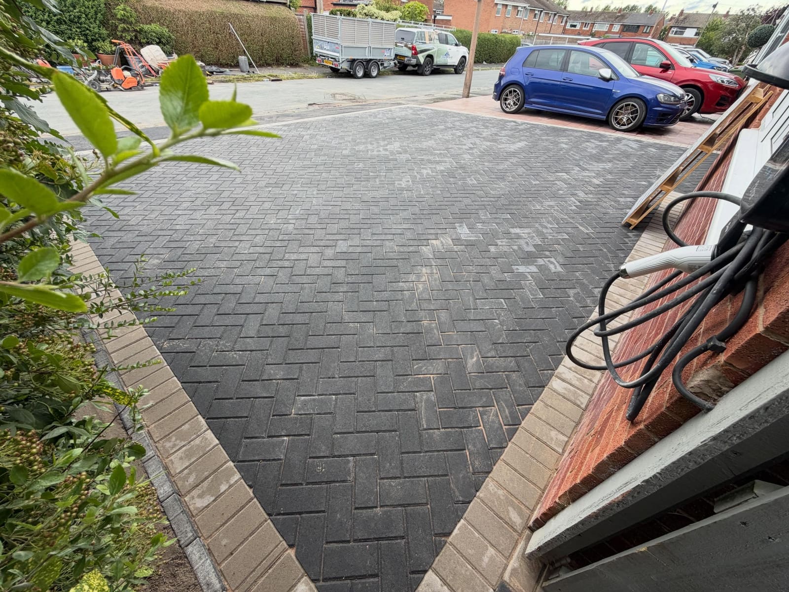 Buff-edged charcoal herringbone driveway beside EV wall charger