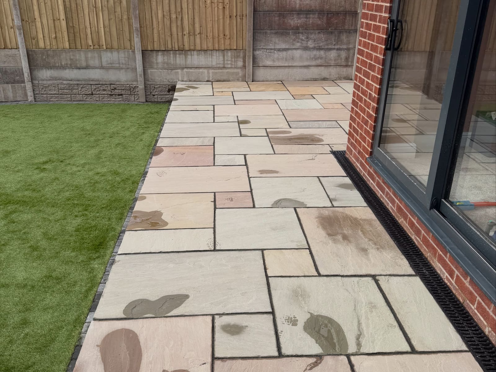 Buff and pink sandstone patio with cobble edger and artificial turf