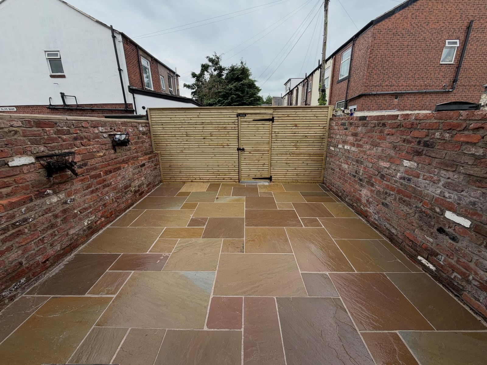 Narrow sandstone courtyard between brick walls with slatted timber gate Cheshire