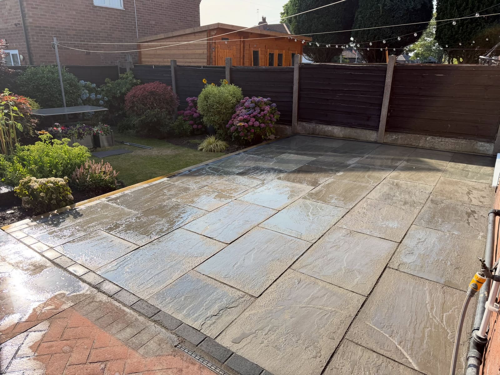 Grey riven sandstone patio with charcoal block border and planted borders