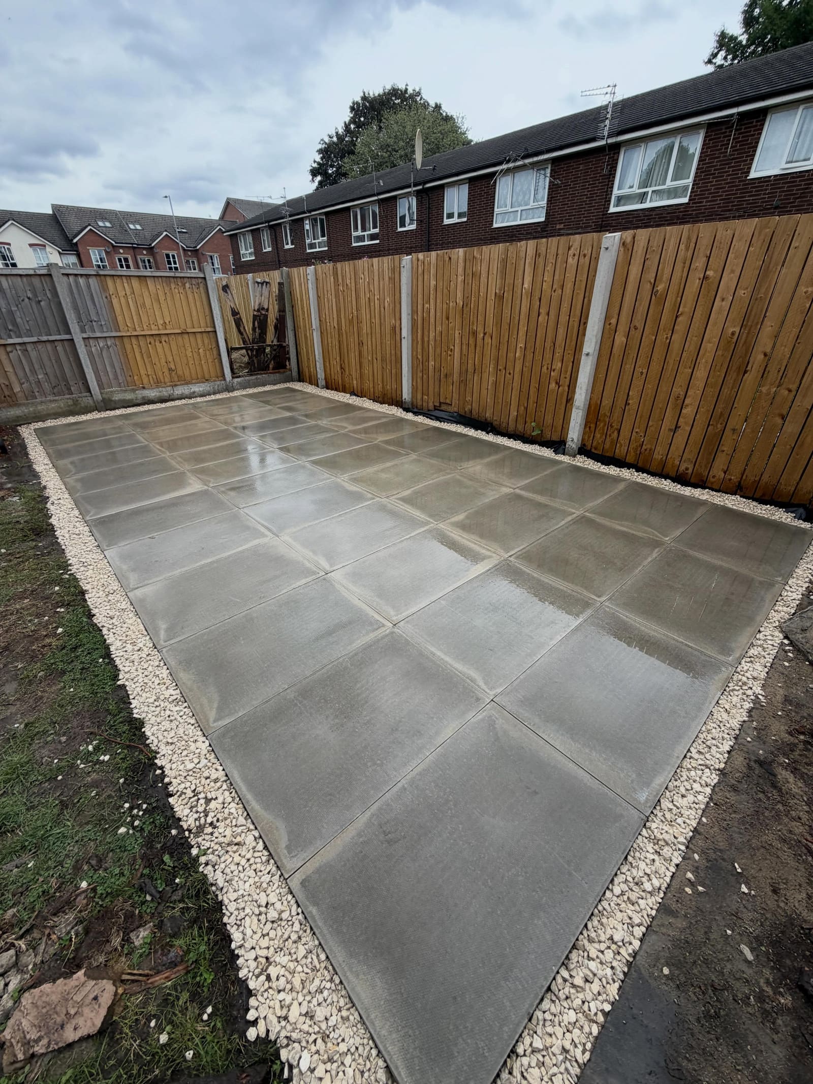 Grid-laid grey paving slabs surrounded by decorative shingle and new fence