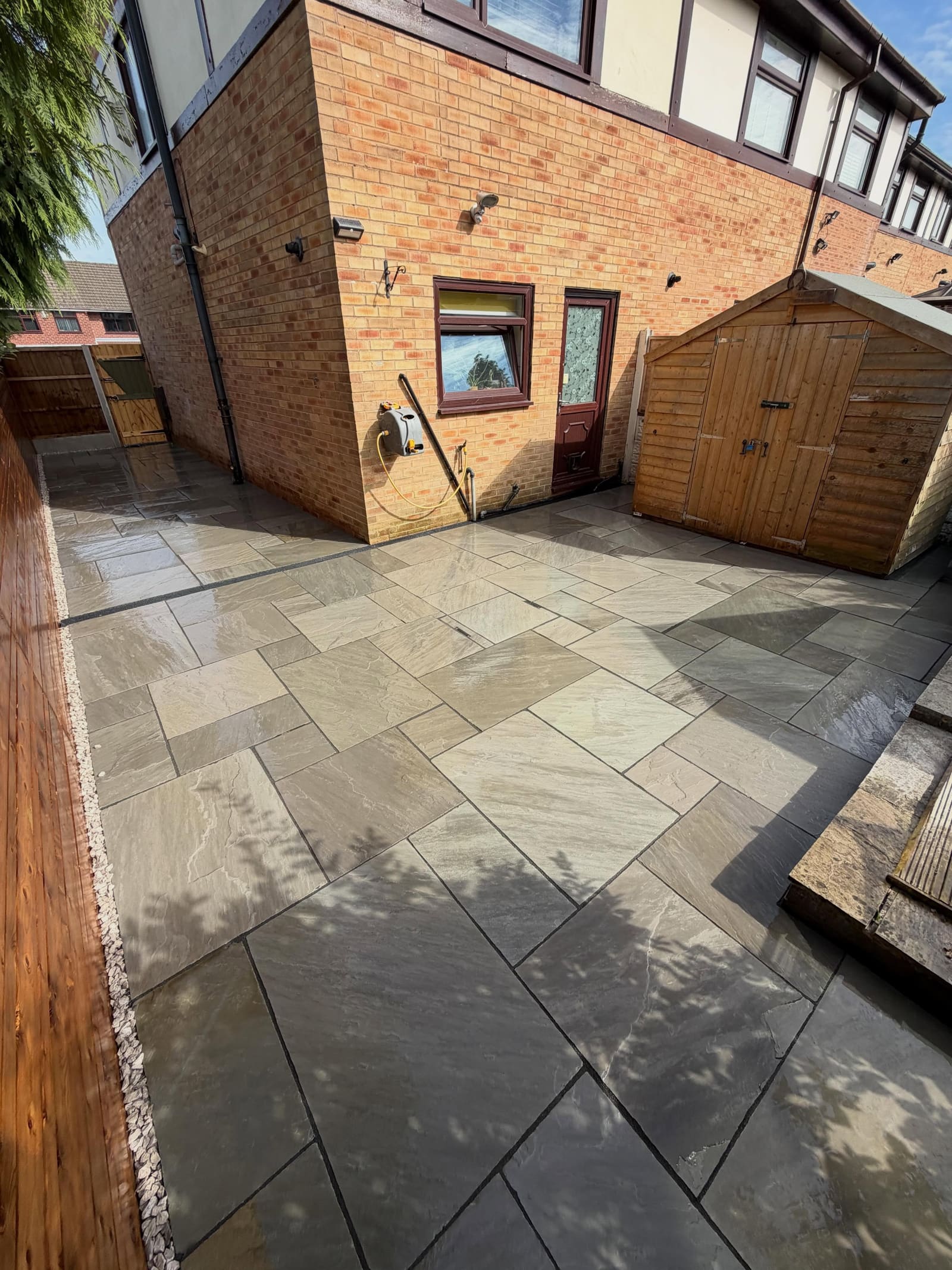 Random pattern Indian sandstone wrapping brick house corner and shed
