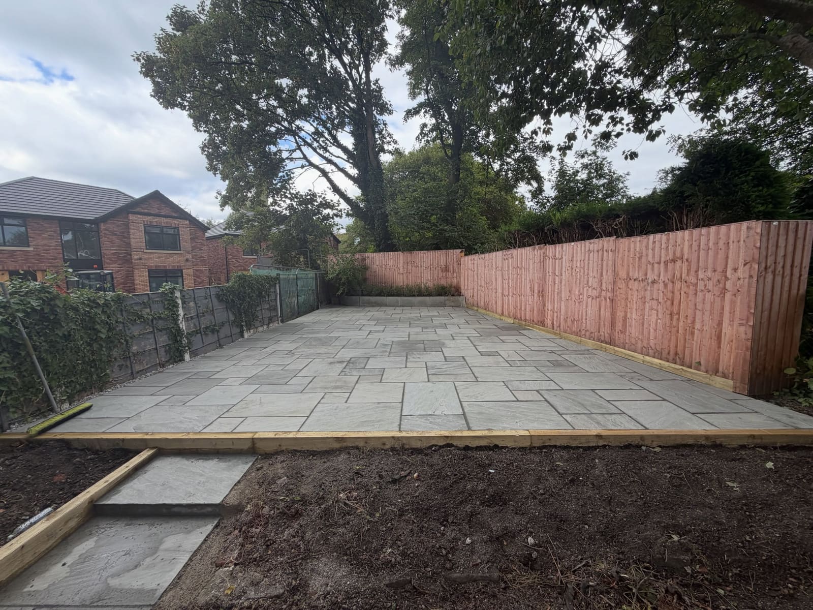 Light grey flagstone patio with timber sleeper border and lap fence