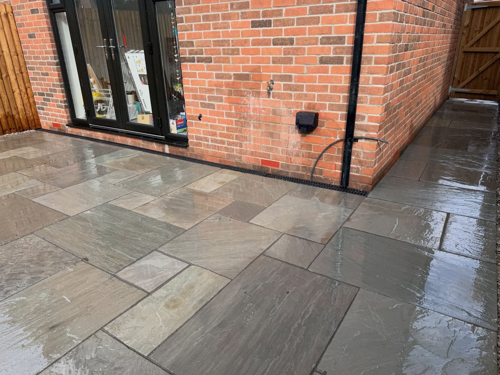 Indian sandstone rear patio with linear drain along red brick wall