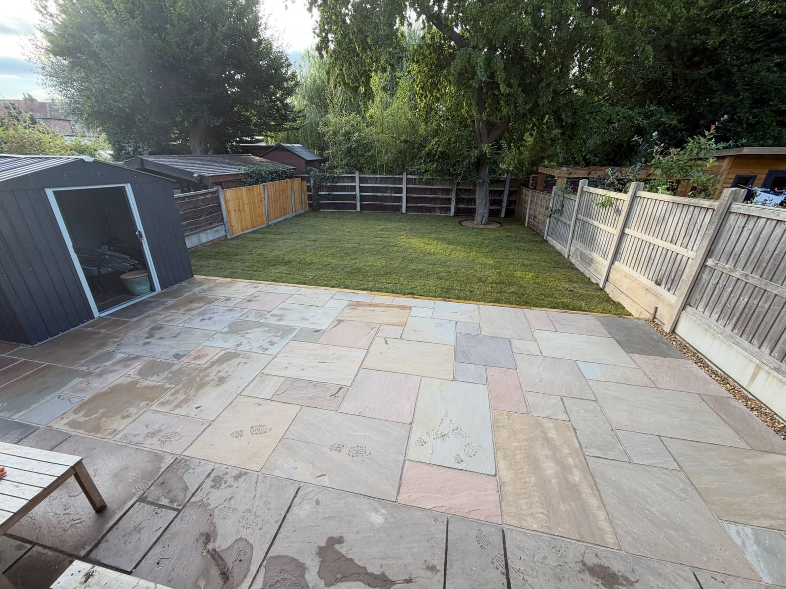 Random laid sandstone flags beside fresh turf and mixed timber fencing Greater Manchester