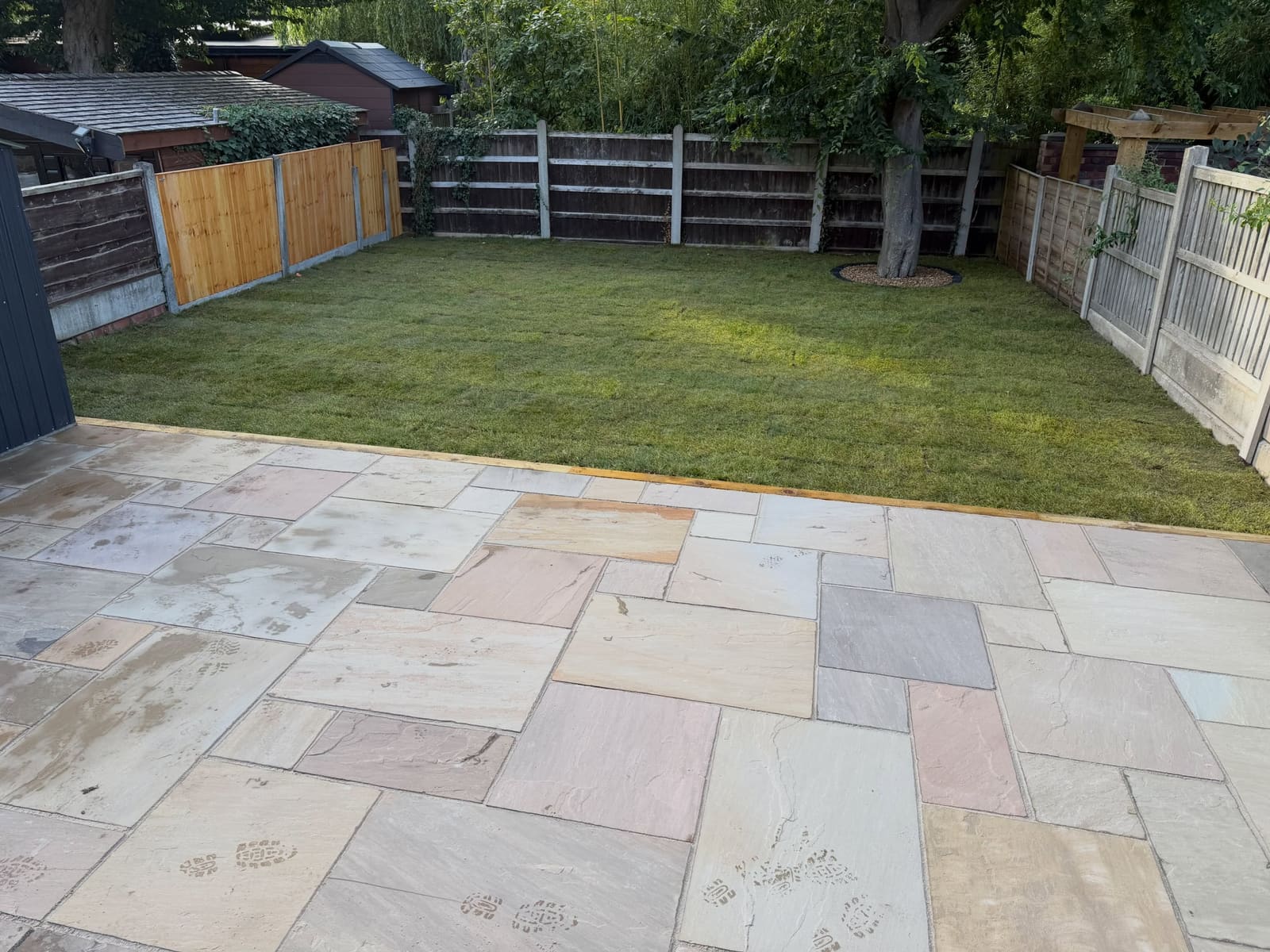 Earthy Indian sandstone patio adjoining newly laid real turf lawn