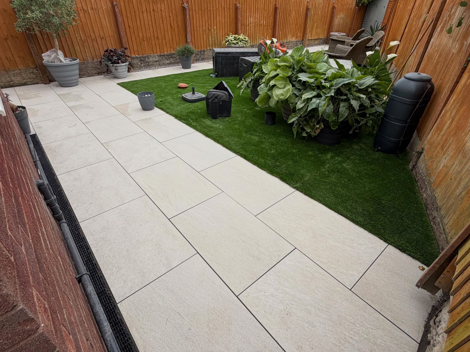 Large-format cream porcelain patio beside artificial lawn and slat fence