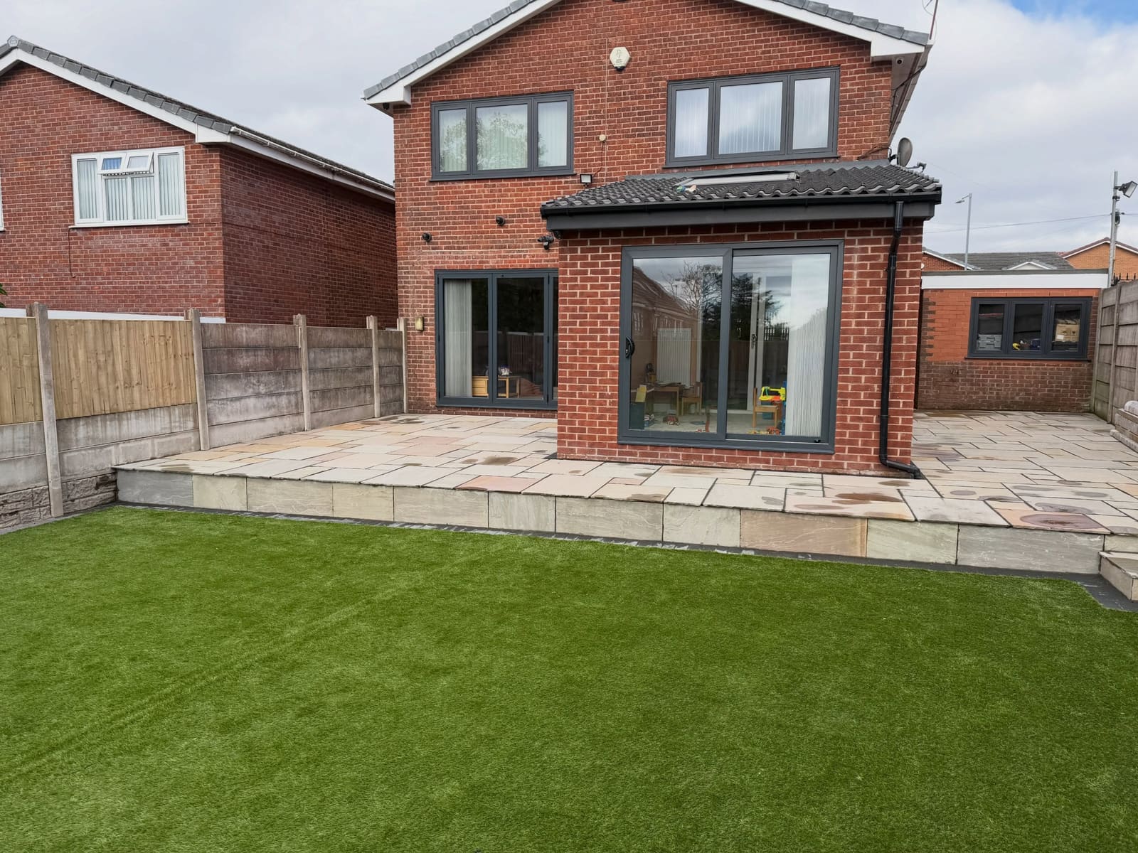 Multi-tonal Indian sandstone patio raised above artificial lawn Cheshire