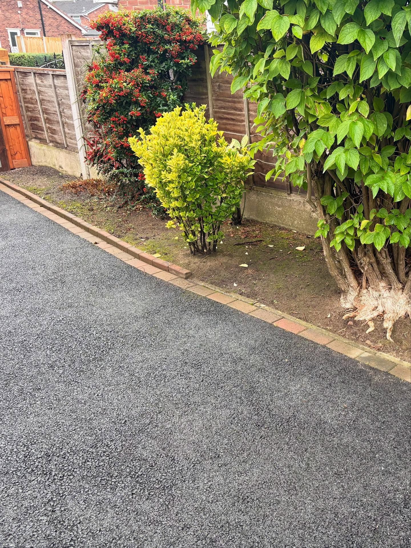 Smooth tarmac drive edged with red block pavers beside garden shrubs Manchester