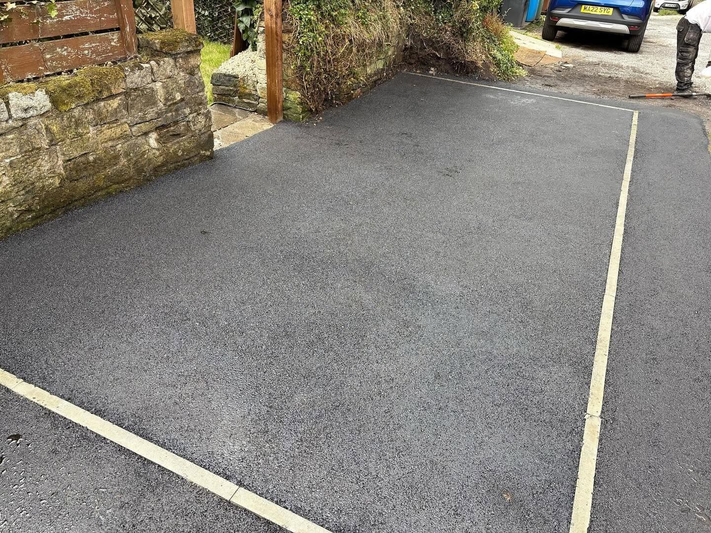 Rectangular tarmac parking area framed by stone kerbs and wall
