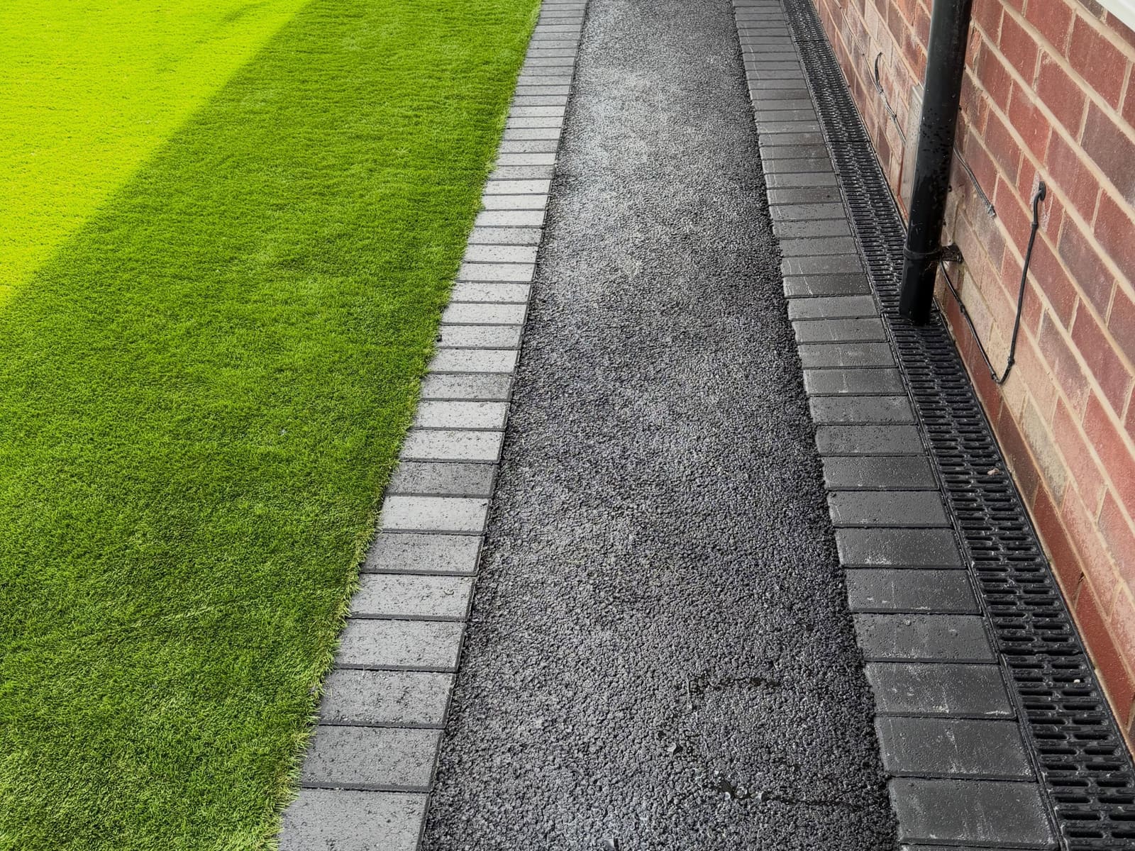 Narrow tarmac path with grey block soldiers and artificial grass lawn