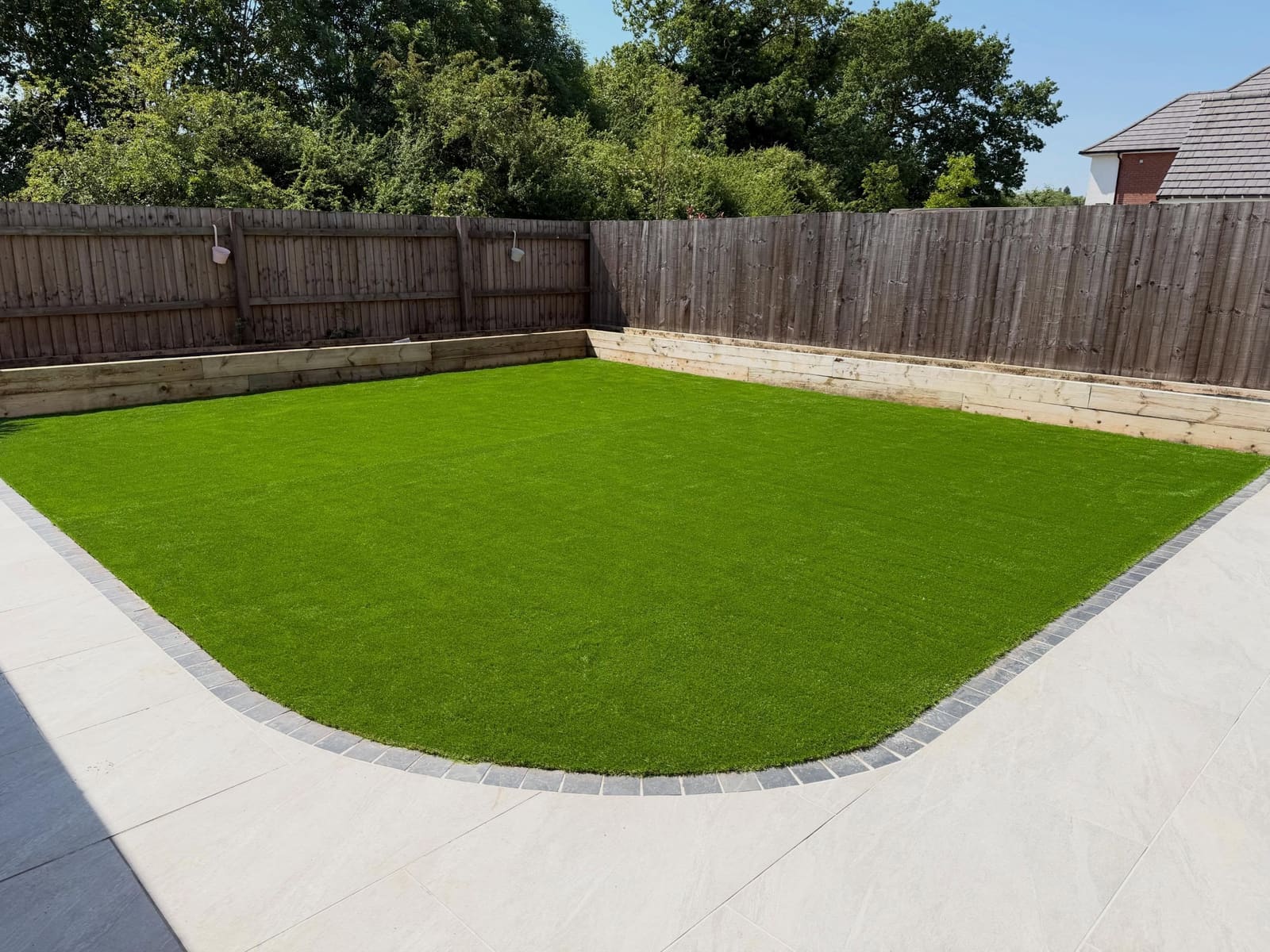 Curved artificial grass beside light porcelain slabs and timber sleeper beds Cheshire