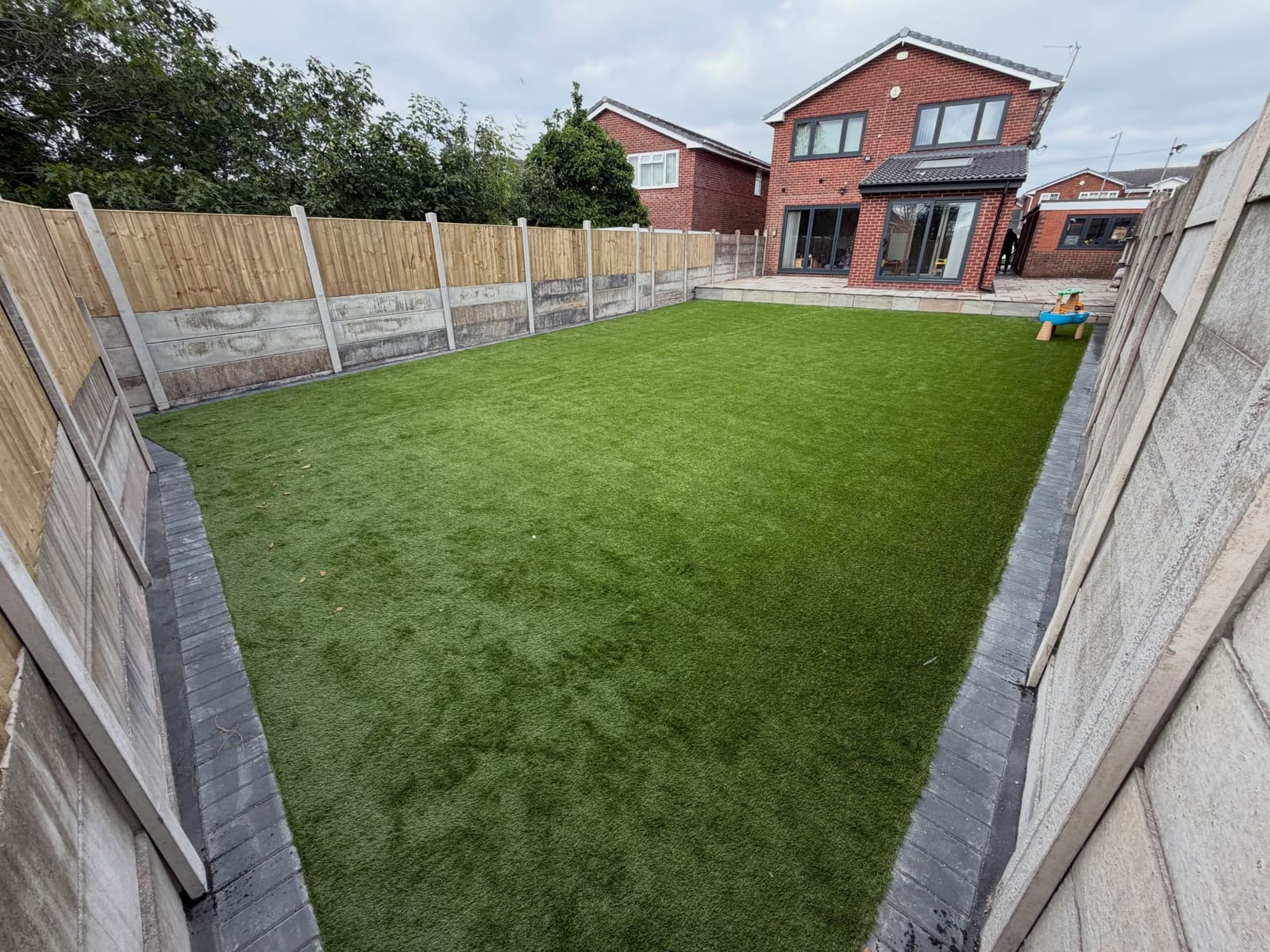 Expansive artificial lawn edged with charcoal block pavers and timber fence Manchester